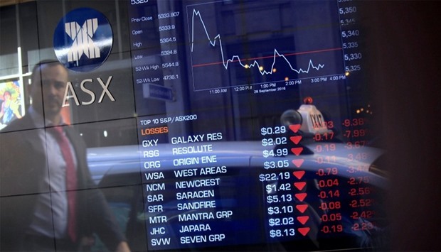 A pedestrian is reflected in a window with a board displaying stock prices