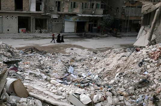 People walk past damaged buildings in the rebel held area of al-Kalaseh neighbourhood of Aleppo, Syria, yesterday.