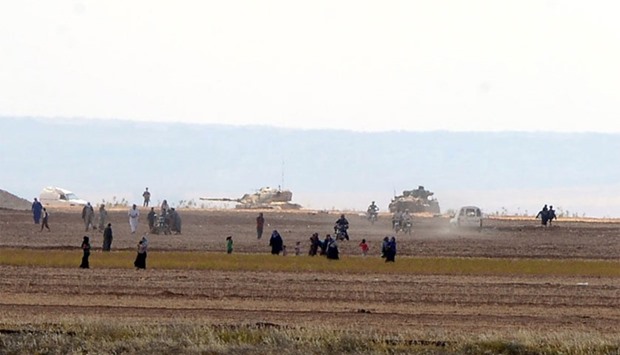 Syrian civilians, with Turkish Army tanks in the background, walk through the Turkish border as they are pictured from a village in Kilis province, Turkey