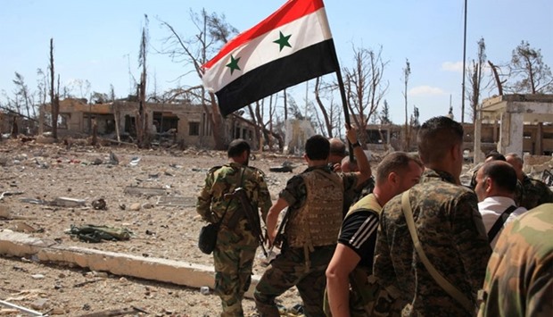 Forces loyal to Syria's President Bashar al-Assad walk at a military complex as one of them holds up a Syrian national flag, after they recaptured areas in southwestern Aleppo on Sunday that rebels had seized last month, Syria