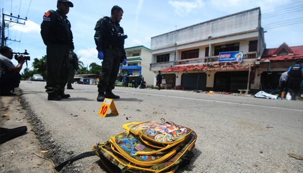 A child's backpack lies on the ground as members of a Thai bomb squad inspect the site of a motocycle blast in front of a school