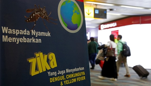 passengers walk past a banner about the Zika virus