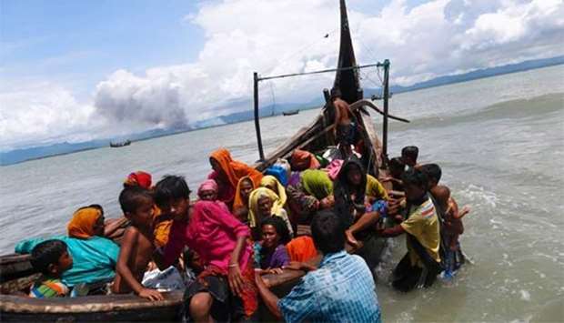 Smoke is seen on Myanmar's side of border as Rohingya refugees get off a boat after crossing the Bangladesh-Myanmar border through the Bay of Bengal in Shah Porir Dwip, Bangladesh on Monday.