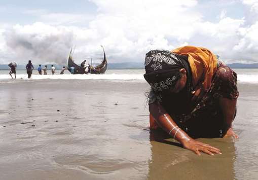 An exhausted Rohingya refugee woman touches the shore after crossing the Bangladesh-Myanmar border by boat through the Bay of Bengal, in Shah Porir Dwip, Bangladesh.