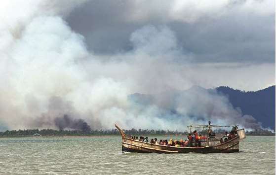 Smoke is seen on Myanmaru2019s side of border as a boat carrying Rohingya refugees arrives on shore after crossing the Bangladesh-Myanmar border through the Bay of Bengal, in Shah Porir Dwip, Bangladesh.