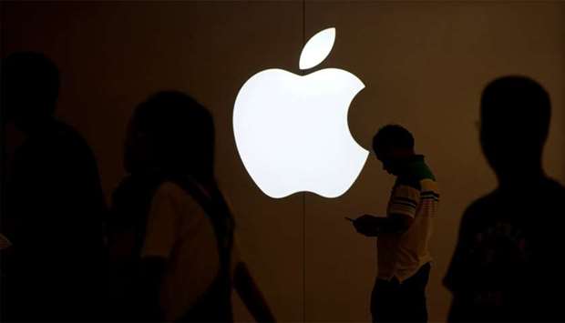 A man looks at the screen of his mobile phone in front of an Apple logo outside its store