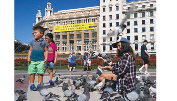A woman and children feed pigeons in Catalonia square in Barcelona in front of a building with a banner reading u2018Yes. Referendum is democracyu2019 on the October 1 referendum on independence.
