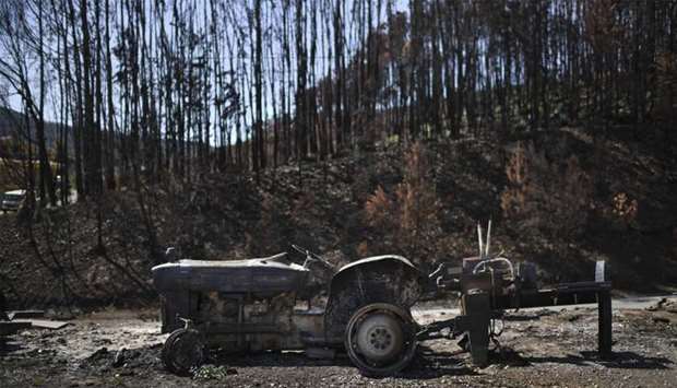 Wreckage of a charred tractor is pictured in front of a burnt forest in Castanheira de Pera