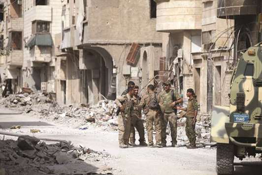 Fighters from Syrian Democratic Forces (SDF) stand together along a damaged street in Raqqa, yesterday.
