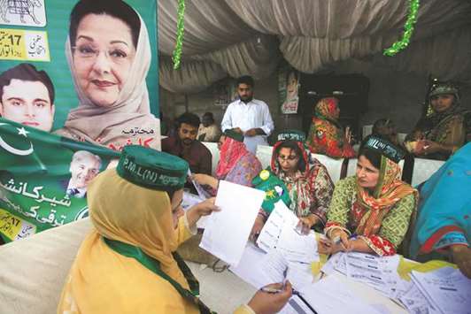 With Kulsoom Nawaz  on the poster, workers of the PMLN political party guide voters and share voting lists before voting in Lahore.