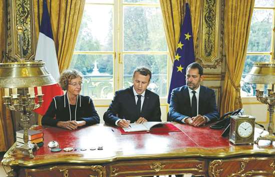 Macron signs documents in front of the media to promulgate a new labour bill in his office at the Elysee Palace. With him are French Labour Minister Muriel Penicaud, and government spokesman and French Junior Minister for the Relations with Parliament Christophe Castaner.