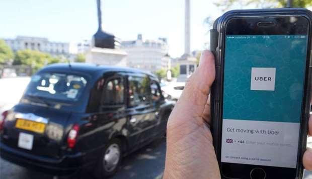 London taxi passing as the Uber app logo is displayed on a mobile telephone