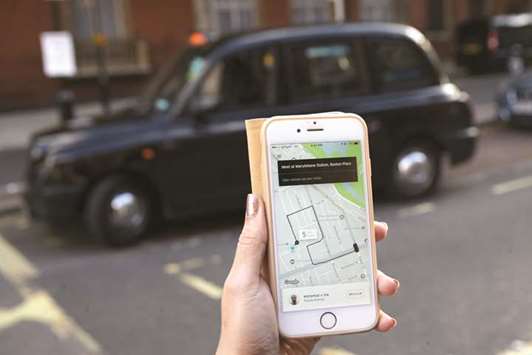 A woman poses holding a smartphone showing the app for ride-sharing cab service Uber in London.