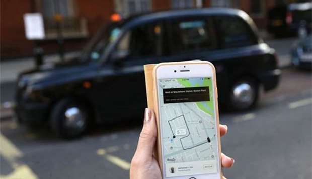 A woman poses holding a smartphone showing the Uber app in London.