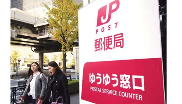 Pedestrians walk past a post office in Tokyo. A government sale of Japan Post Holdings Co stock raised $11bn in the worldu2019s second-biggest share sale this year.