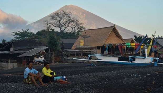 Mount Agung looms in the background at dawn as locals sit near huts and fishing boats at Amed beach, one of the nearest tourist resorts from the volcano, in Karangasem on the island of Bali on Wednesday.
