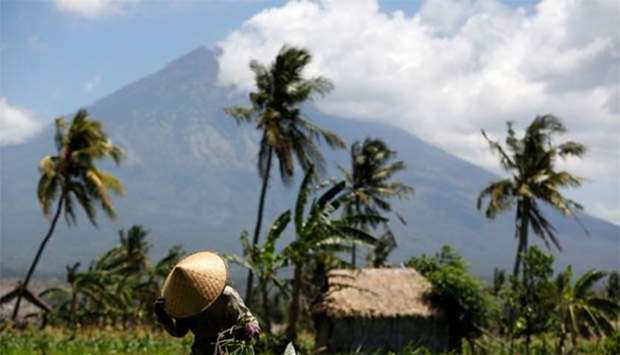 Mount Agung, a volcano which had its alert status raised to the highest level last week, is seen as a farmer tends her crops, near Amed, on the resort island of Bali, on Friday.