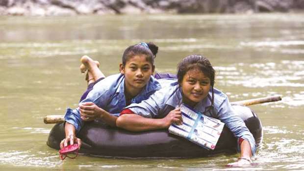 Students use their sandals to paddle across the Trishuli river on a float to reach school each day in Dhading district.