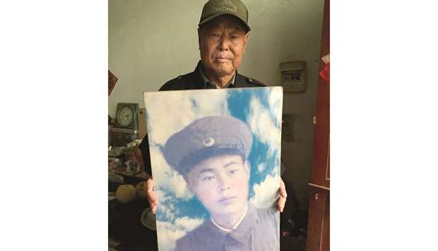 Xiao with a portrait of himself as a young soldier in the Chinese army in the 1950s.