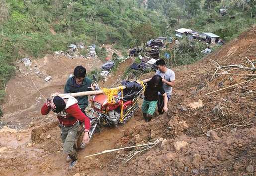Residents carry a motorcycle as they hike on a road eroded by a landslide caused by the typhoon at a small-scale mining camp in Itogon, Benguet.