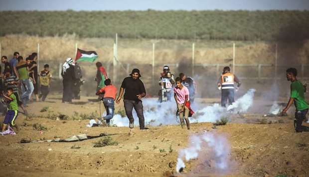 Palestinian protesters run for cover from incoming teargas grenades during clashes with Israeli forces following a demonstration along the border fence east of Gaza City, yesterday.