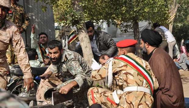 Soldiers and a Shia Muslim cleric (R) sitting close to the ground seeking cover at the scene of an attack on a military parade.