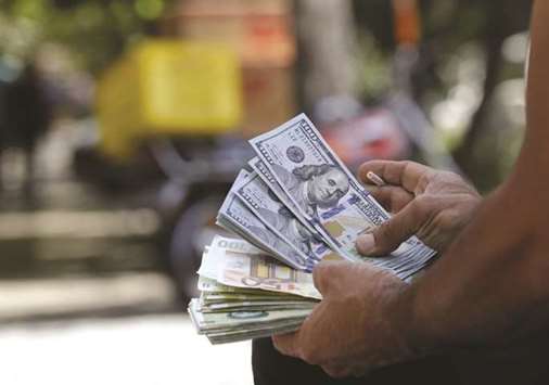 A man holds a stack of Iranian rials and US dollars in the Iranian capital Tehran. With old US sanctions resuming, the rial went into free fall on Tehranu2019s black market. Panicked businesses and individuals snapped up increasingly scarce dollars, forcing the central bank to impose capital controls.