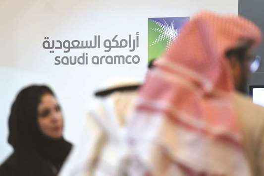 Saudi and foreign investors stand in front of the logo of state oil firm Aramco during a business forum in the capital Riyadh. The Aramco IPO delay reflects complexities the government faces in opening up the public sector.