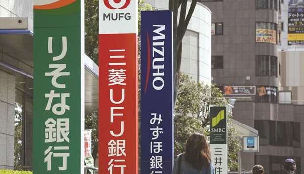 Pedestrians walk past signage for (from left) Resona Bank; MUFG Bank, the main banking unit of Mitsubishi UFJ Financial Group; Mizuho Bank; and Sumitomo Mitsui Banking Corp in Tokyo (file). Asiau2019s lenders including Mitsubishi UFJ Financial Group and KB Financial Group are being pressured, with shares suffering from ultra-low interest rates in Japan eating into profit margins, the Trump Administrationu2019s tariffs, Chinau2019s deleveraging efforts and an ongoing investigation of Australiau2019s banking industry.