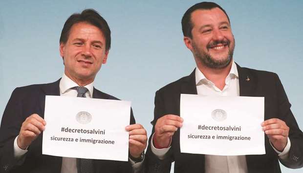 Prime Minister Conte and Interior Minister Salvini hold up pieces of paper with the name of the new decree written on them, during a news conference at Chigi Palace in Rome.