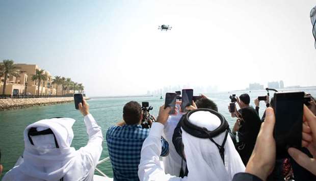 Attendees of Ooredoo's 5G technologies test on Wednesday taking pictures and videos of the worlds-first Self-Driving 5G connected Aerial Taxi as it flies over The Pearl-Qatar. The large drone-like vehicle can transport two people to a destination up to 20 minutes away with a 130 Km/h speed. The taxi is automatic and runs on Ooredoou2019s 5G network.