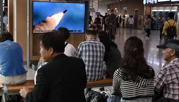 People watch a television news screen showing file footage of a North Korean missile launch, at a railway station