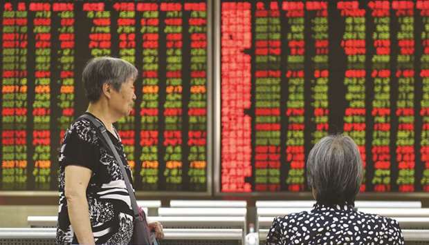 Women talk in front of a screen showing stock prices at a securities firm in Beijing. The Shanghai index slipped 0.1% to 3,021.20 points yesterday.