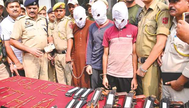 Kathua police personnel stand next to three men with their faces covered and with weapons and ammunition recovered after their arrest in Kathua. The men were arrested yesterday transporting arms to Kashmir.