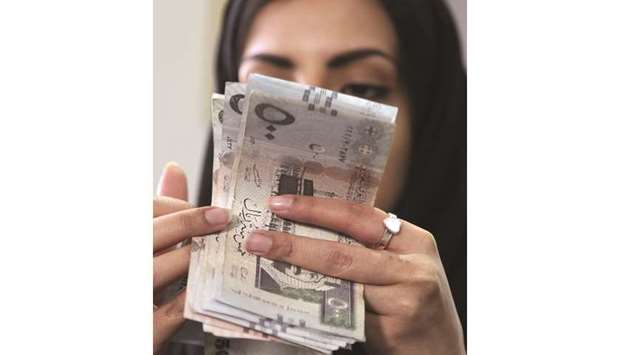 A Saudi woman counts Saudi riyal banknotes at a money exchange shop in Riyadh (file). Forwards contracts on the riyal yesterday headed for the biggest jump in more than four years on the prospect of a dollar squeeze, and Saudi Aramcou2019s dollar notes also fell.