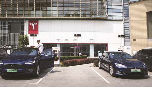 A man cleans a Tesla Model X electric vehicle connected to a charging station outside one of the companyu2019s showrooms in Beijing. Tesla is among automakers most affected by the US-China trade tensions, because it has no local production yet and therefore gets directly hit by any increases in tariffs.