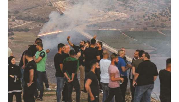 People flash the victory gesture as they pose for a u201cselfieu201d photo on a cell phone while others watch as fires blaze along the Lebanese side of the border with Israel in the Lebanese village of Maroun al-Ras, yesterday, following an exchange of fire between Hezbollah and Israel.