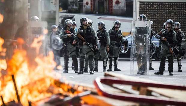 Police in riot gear stand watch past a burning barricade during clashes with pro-democracy demonstrators in Hong Kong's Tuen Mun district