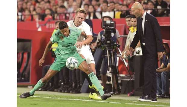 Real Madrid coach Zinedine Zidane (right) looks on as his defender Raphael Varane (left) and Sevillau2019s Luuk De Jong fight for the ball during the La Liga match at the Ramon Sanchez Pizjuan stadium in Seville on Sunday. (AFP)