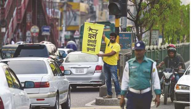 Mominur Rahman Royal holds a banner with a Bengali slogan - u201cHorn hudai, Bajay Bhudaiu201d that translates to u201conly the idiot honks horn unnecessarilyu201d - on a busy street in Dhaka.