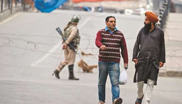 Men walk past security personnel during strict restrictions in Srinagar yesterday.