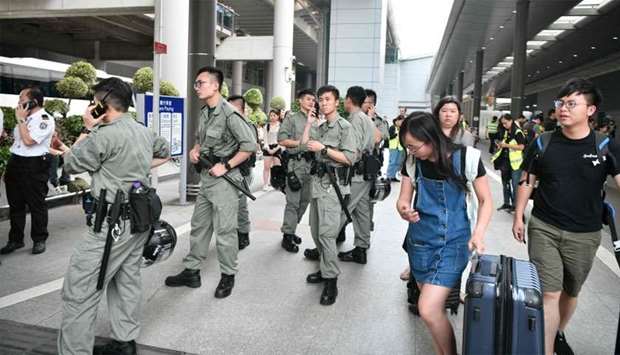 Passengers roll their luggage past police outside Chek Lap Kok International Airport in Hong Kong