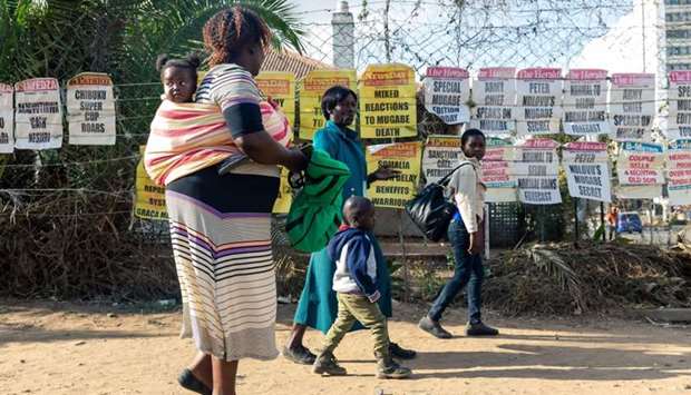 Pedestrians walk past signs of the various daily newspapers on the streets of Harare on September 7 2019, on the first day of a period of national mourning following the death of former Zimbabwe president Robert Mugabe