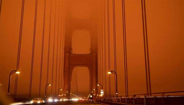 Cars drive along the Golden Gate Bridge under an orange smoke filled sky at midday in San Francisco, California