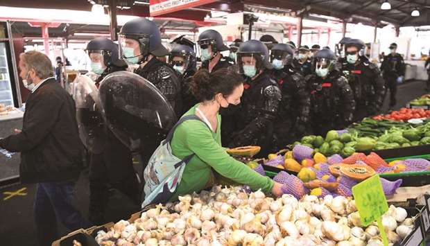 A woman continues to shop for vegetables as riot police clear Melbourne's Queen Victoria Market of a