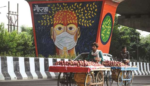 Fruit vendors push their hand carts past a coronavirus-themed mural painted on a pillar of a flyover in Noida yesterday.