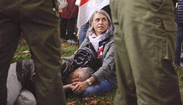 A woman sits with a man lying on the ground near Belarusian law enforcement officers during an opposition rally in Minsk to protest police brutality and to reject the presidential election results.