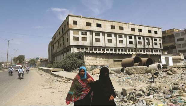 Women walk along a road in Karachi, with an abandoned building that housed a garment factory in the background, where more than 260 people died in a fire broke in 2012.