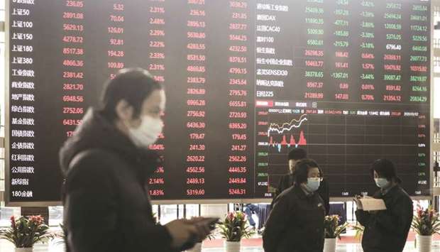 Employees and visitors wearing protective masks walk past an electronic stock board at the Shanghai Stock Exchange. The Composite index closed up 0.2% to 3,224.36 points yesterday.