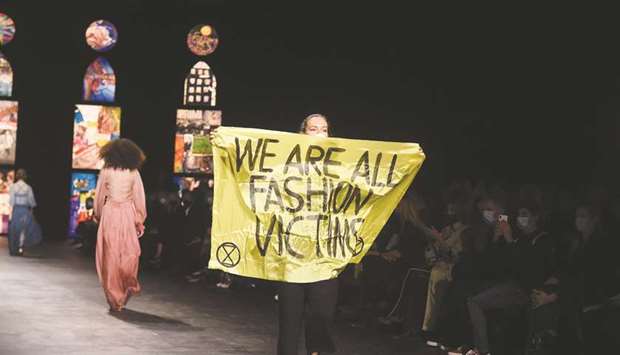 An Extinction Rebellion activist holds a sign as a model presents a creation by Dior during the Paris Fashion Weeku2019s Women Spring Summer 2021 ready-to-wear  fashion show.
